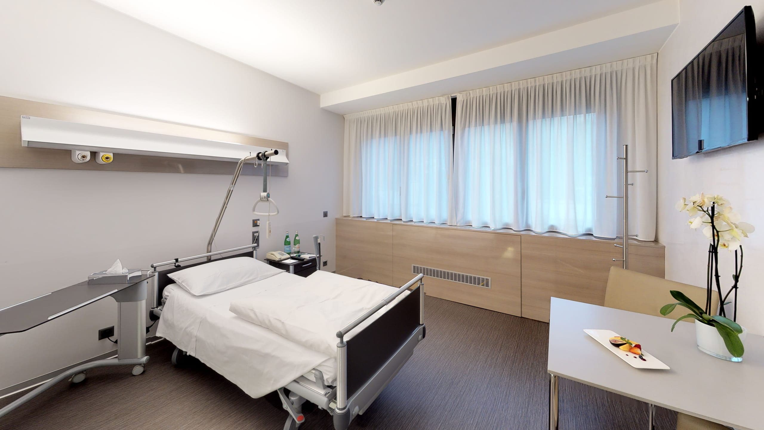 Camera di degenza della Clinica Ars Medica con letto di cura e rivestimento in legno chiaro.