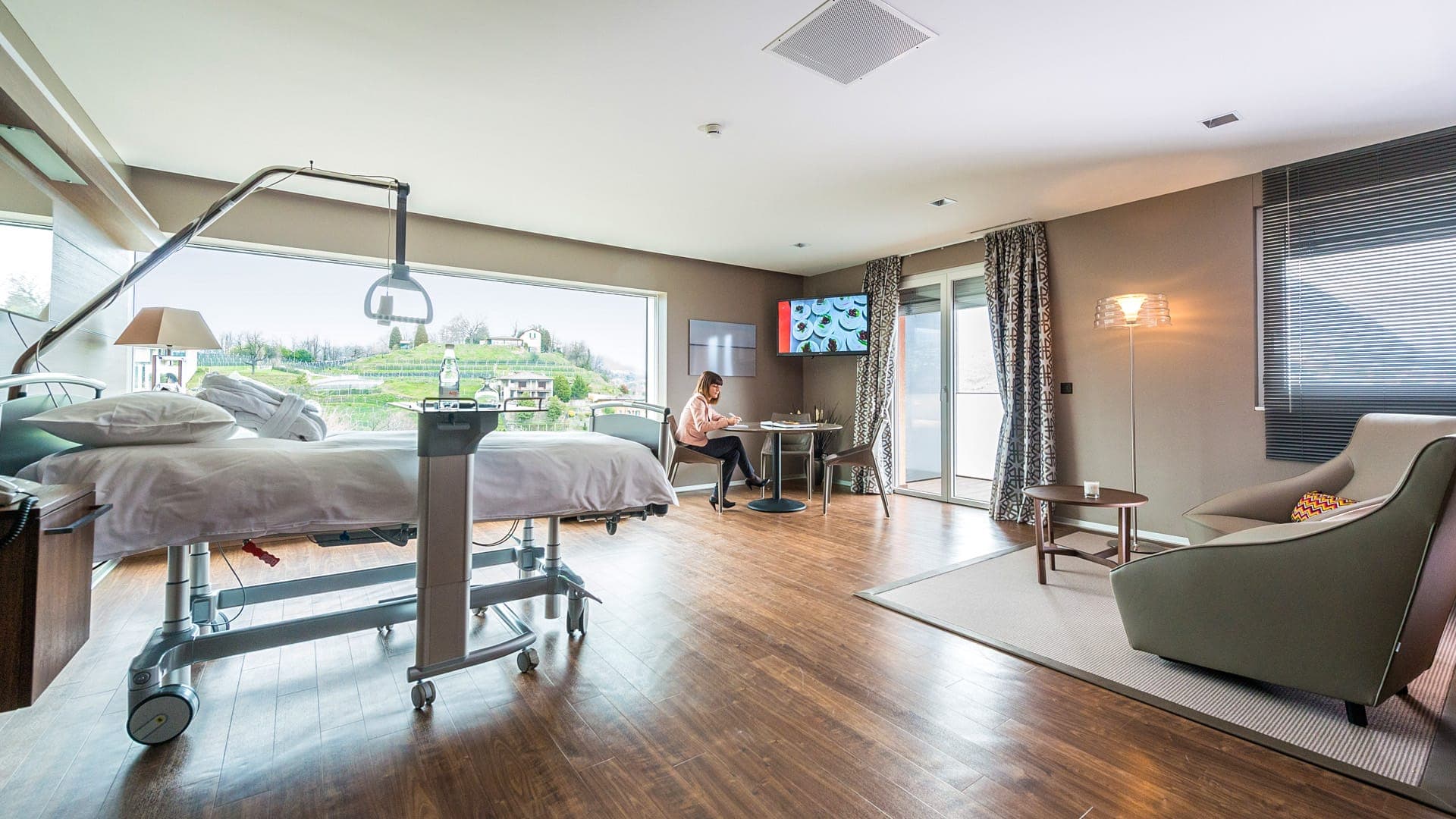 Sala parto della Clinica Sant’Anna con letto di cura, salottino e TV a parete.