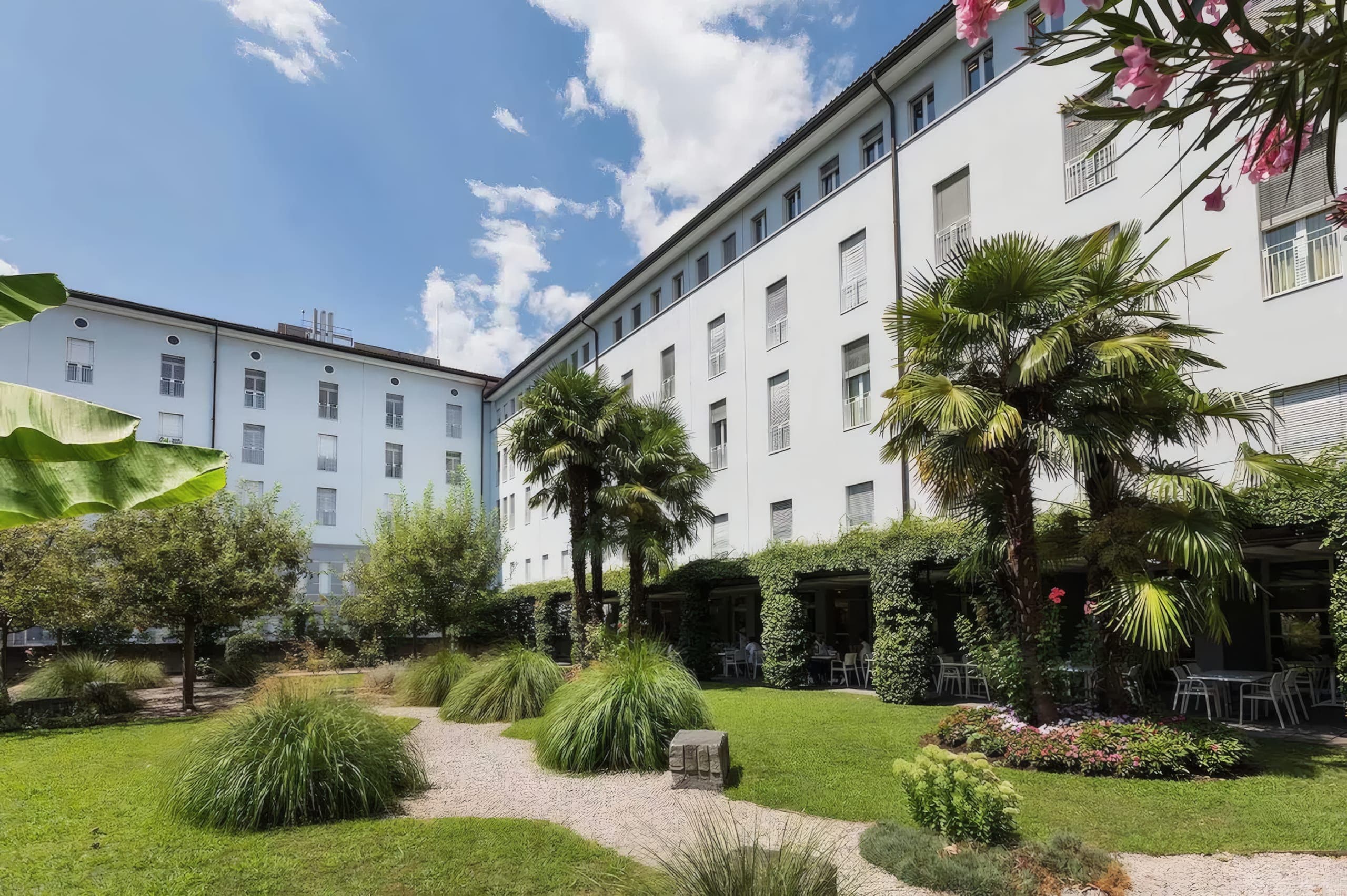 Corte giardino dell’Ospedale La Carità di Locarno con palme davanti all’edificio bianco.