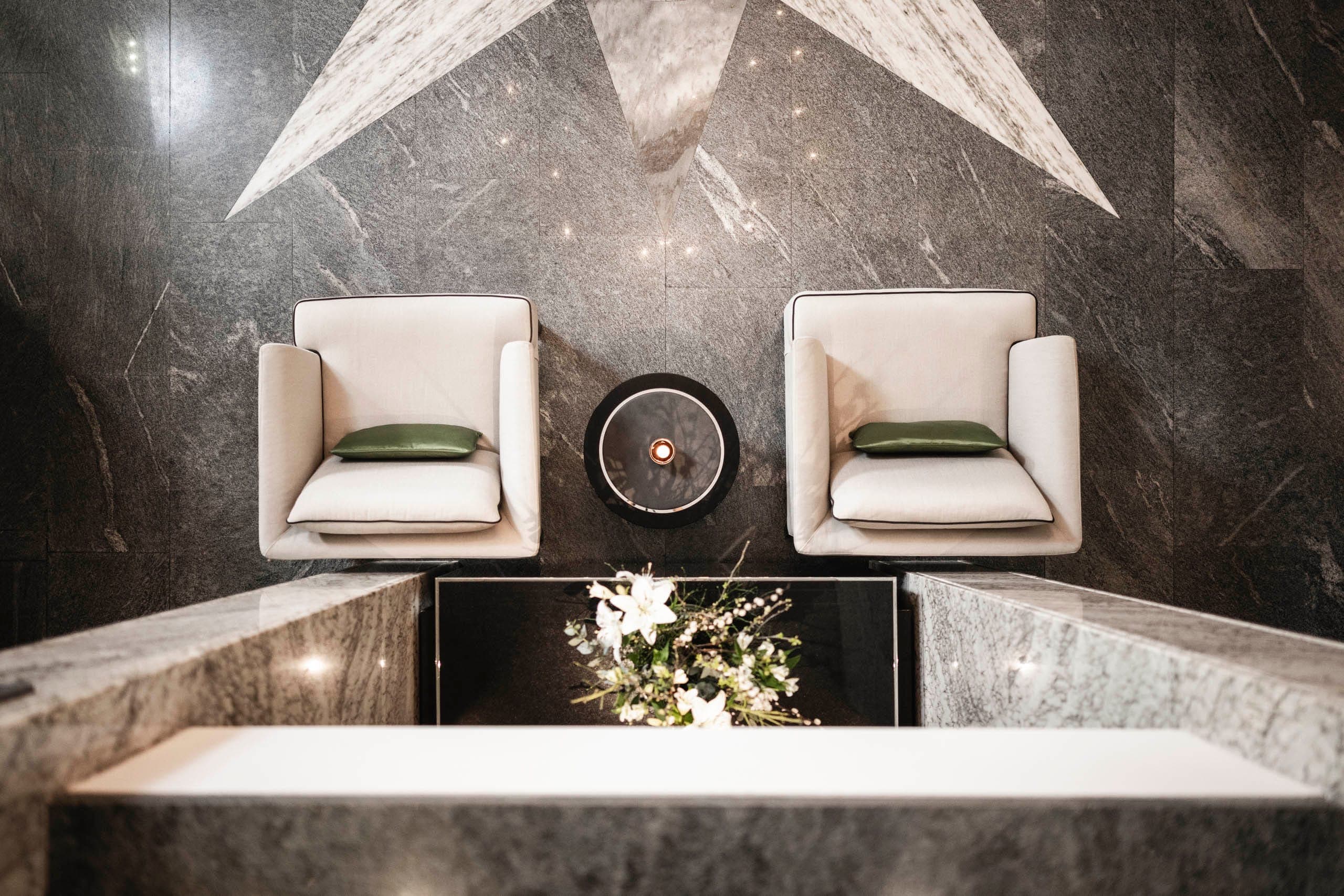 Lounge dell’Hotel Belvedere a Locarno con due poltrone chiare davanti a una parete in pietra naturale.