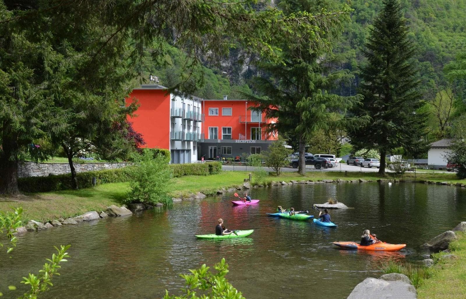Motel-Ristorante Afia a Cama dietro il laghetto con i kayak, sullo sfondo i pendii boscosi della Mesolcina.