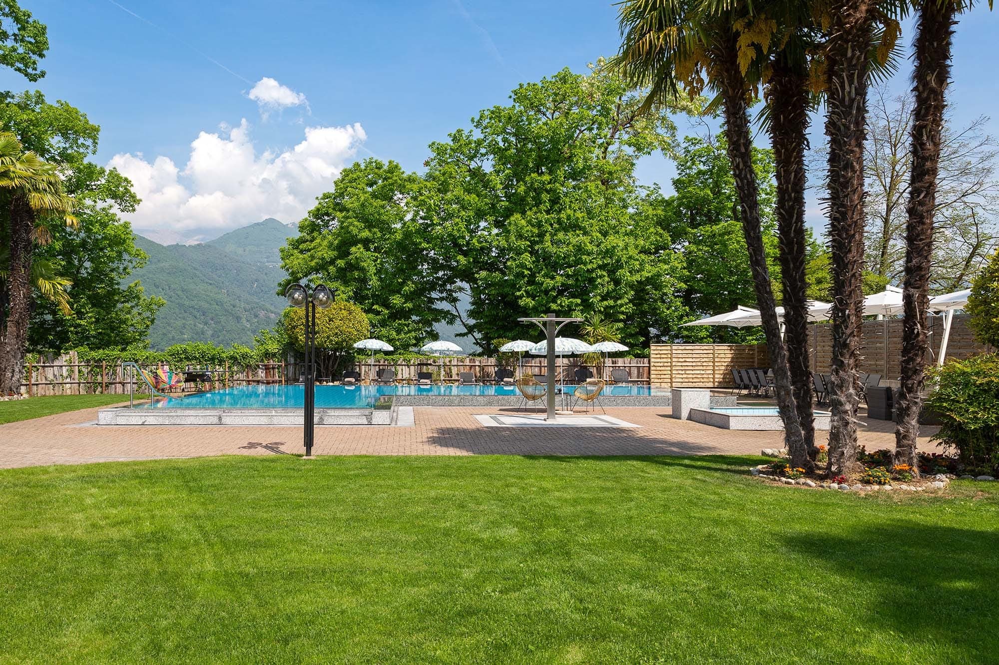 Giardino con piscina del Resort al Centro, palme e panorama montano a Breganzona.