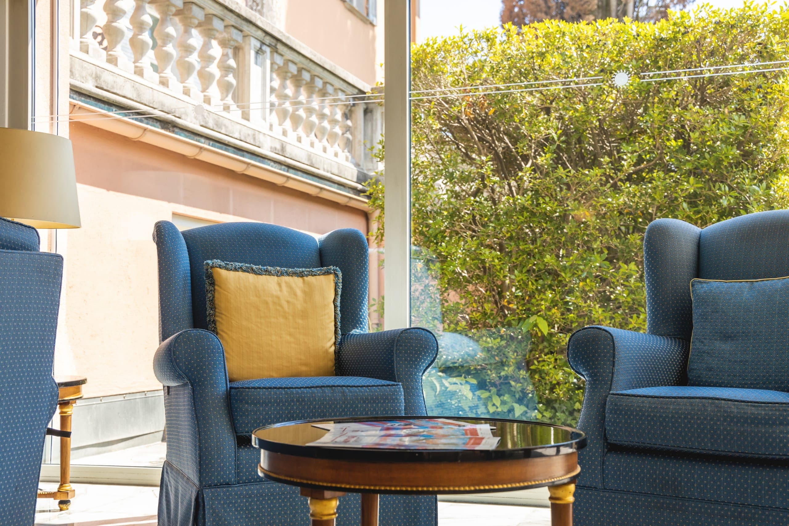 Salotto di Villa Sassa a Lugano con poltrone blu e finestra a tutta altezza sul giardino.