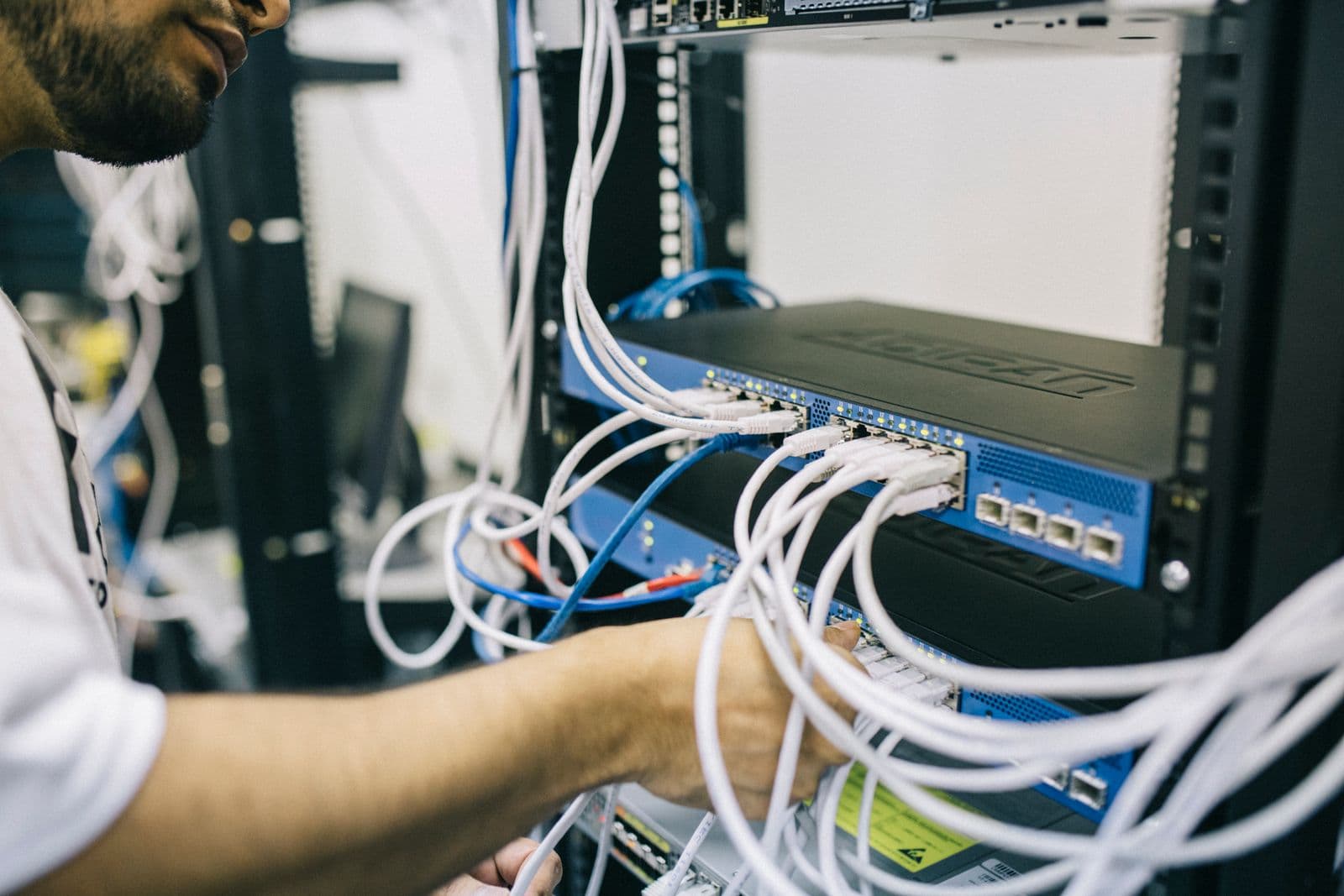 Techniker steckt Patchkabel in einen Netzwerk-Switch im offenen Serverschrank.