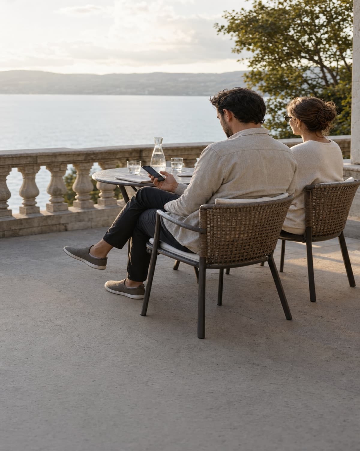 Terrazza d’hotel sopra il lago con due ospiti al tavolo nella luce della sera.
